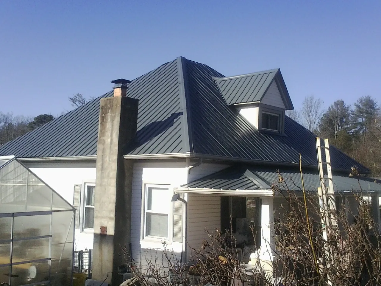 Dark blue standing seam metal roof on a white farmhouse with dormer — Slate & Tile Roof Repair by Roofing Brothers in Cedar Valley