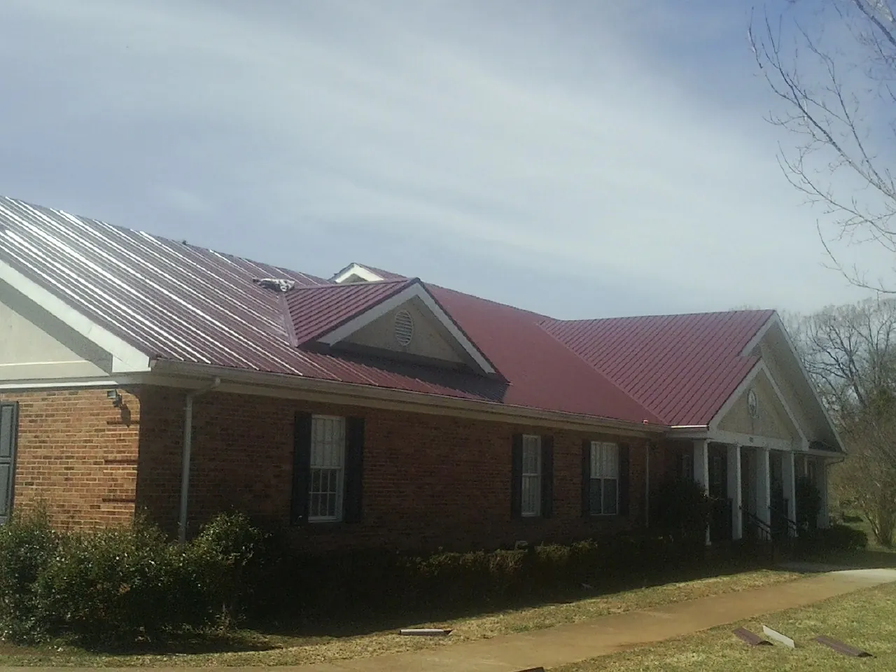 Red metal roof with gabled entries on a long brick building, from a Hail Damage Roof Repair job in Cedar Valley