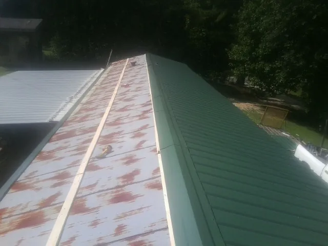 Old rusted panels beside newly installed green metal roofing — Wind Damage Roof Repair by Roofing Brothers in Cedar Valley