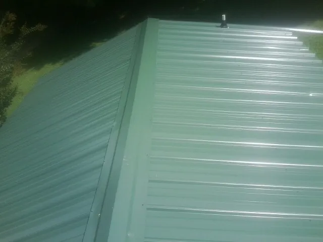 New green metal panels meeting at the ridge of a roof — Flat Roof Repair work by our crew in Cedar Valley