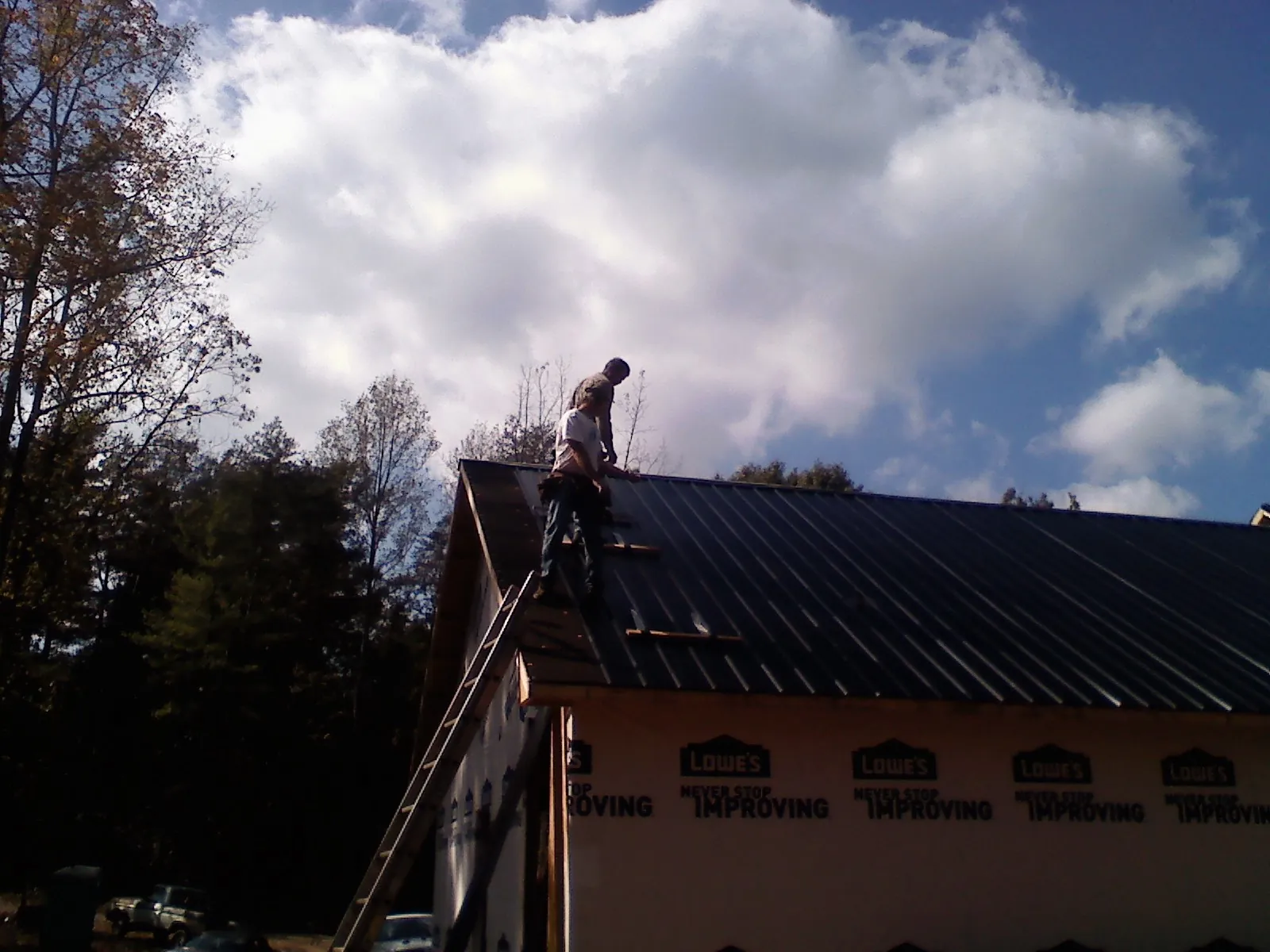 Roofer fastening dark metal panels high against a cloudy sky, from a Roof Inspection job in Cedar Valley