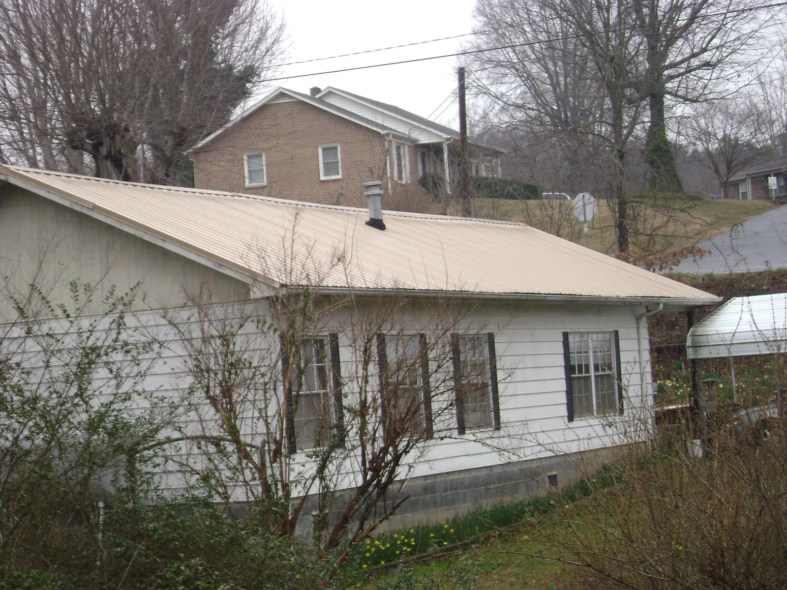 Tan metal roof on a white sided house set into a hillside — Commercial Roofing by Roofing Brothers in Cedar Valley